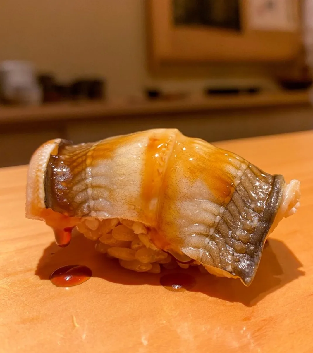Tender anago nigiri brushed with glossy tsume sauce at a sushi counter