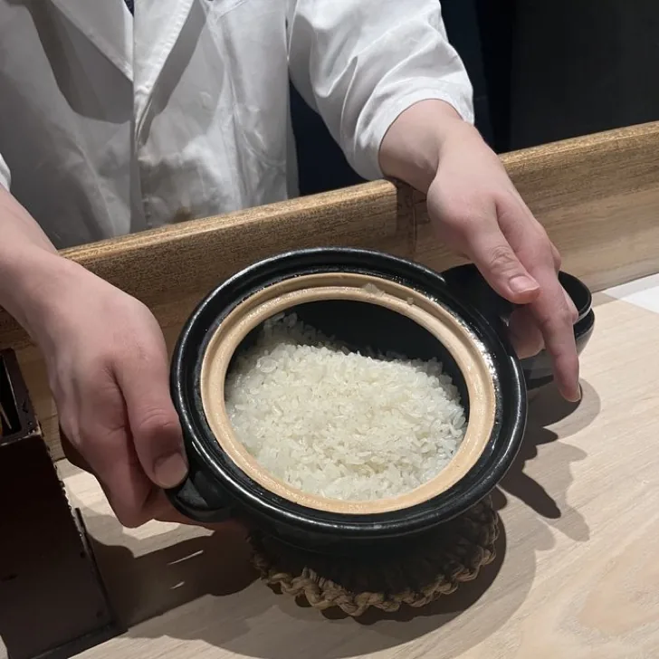 presenting freshly cooked white rice in a small black donabe at a Japanese counter