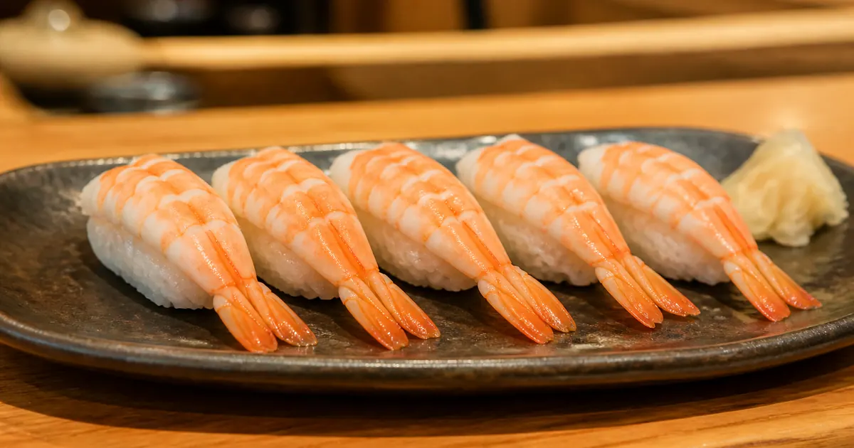 Five pieces of cooked shrimp nigiri on a ceramic plate