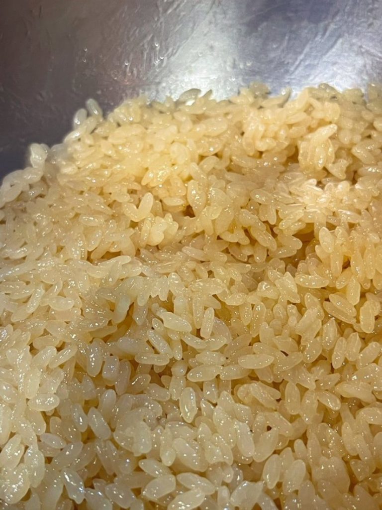 Glossy seasoned sushi rice with a light amber color in a stainless-steel mixing bowl