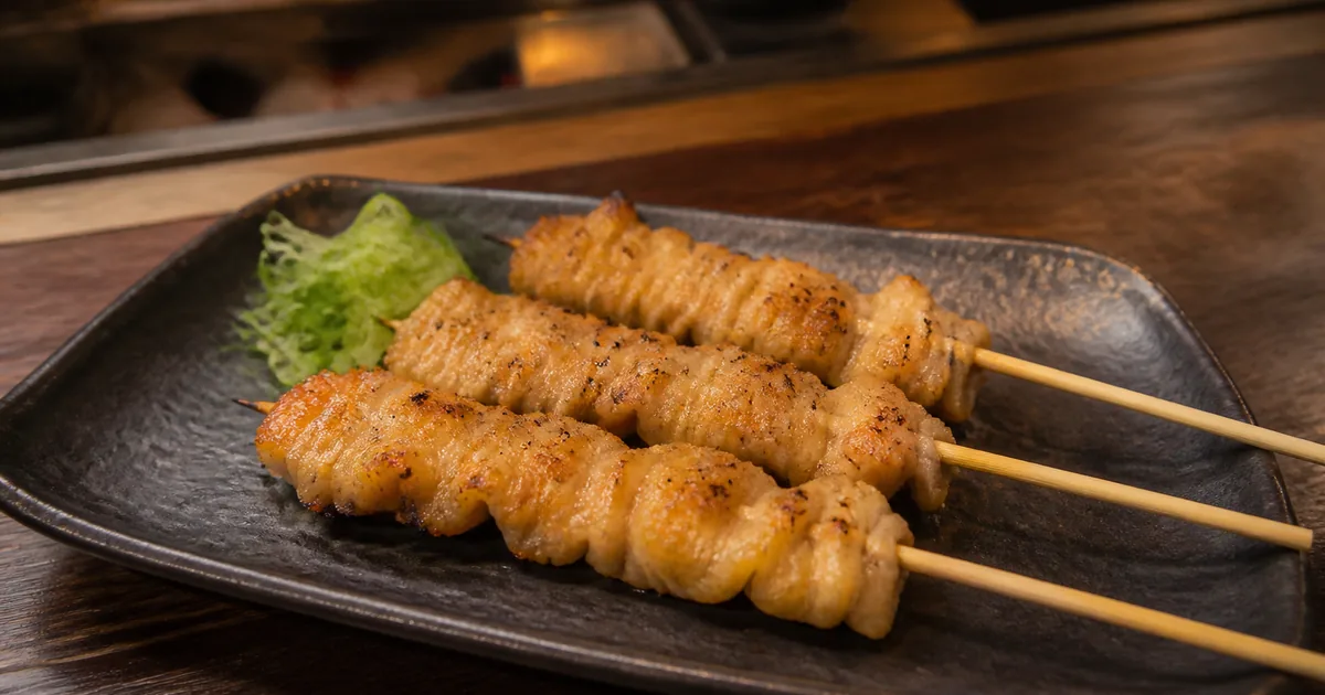Three grilled kawa chicken skin skewers on a dark ceramic plate
