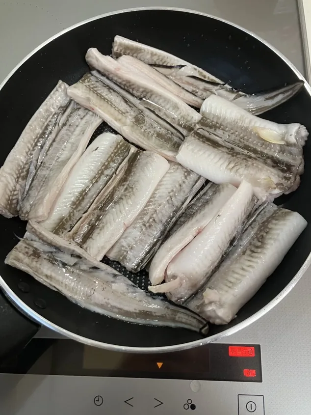 Cleaned anago fillets arranged in a wide pan before simmering