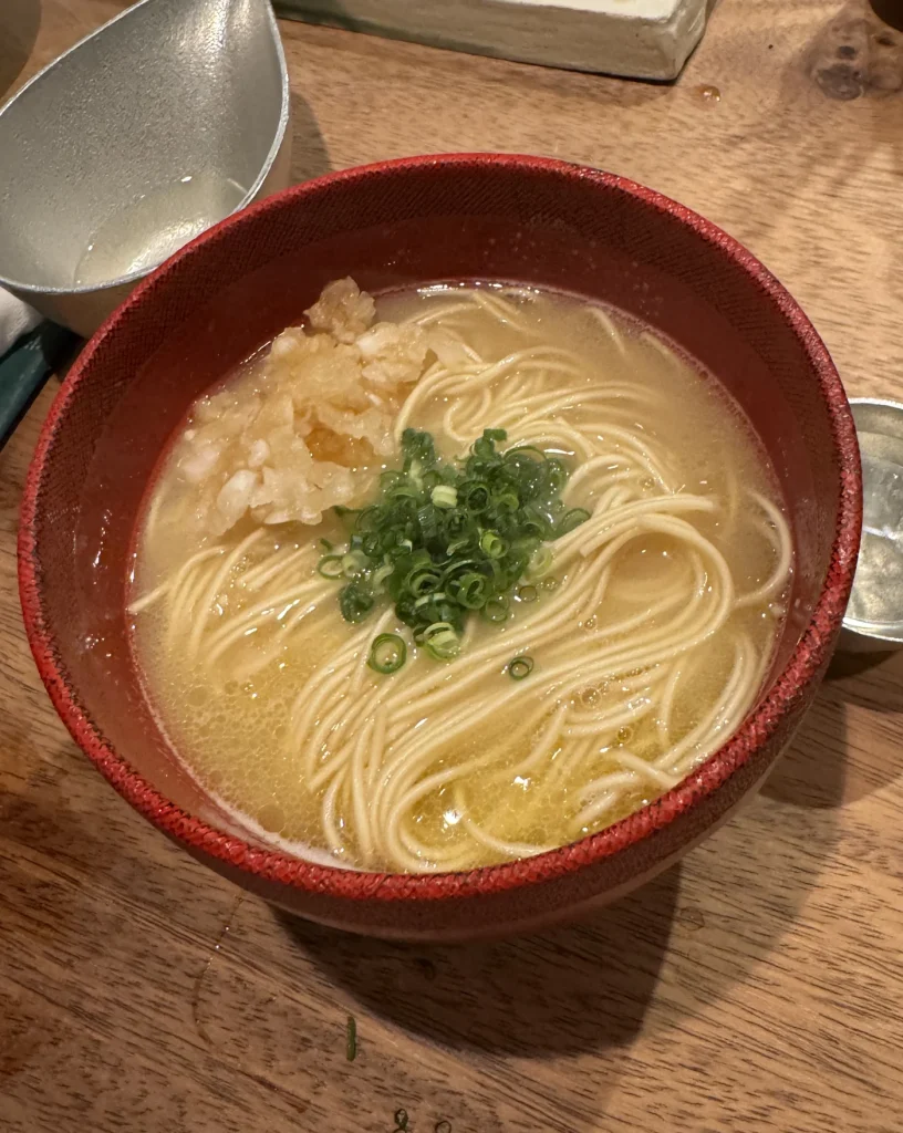 Rich cloudy ramen with thin noodles, chopped onions, and green onions in a red bowl