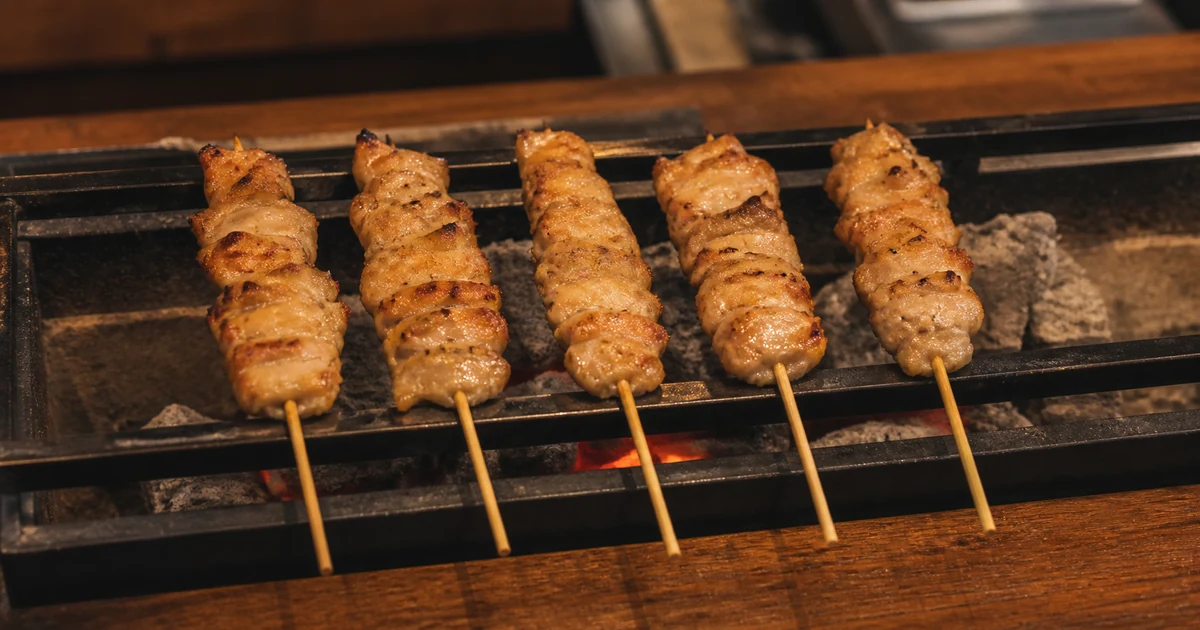 Five momo yakitori chicken thigh skewers grilling over charcoal