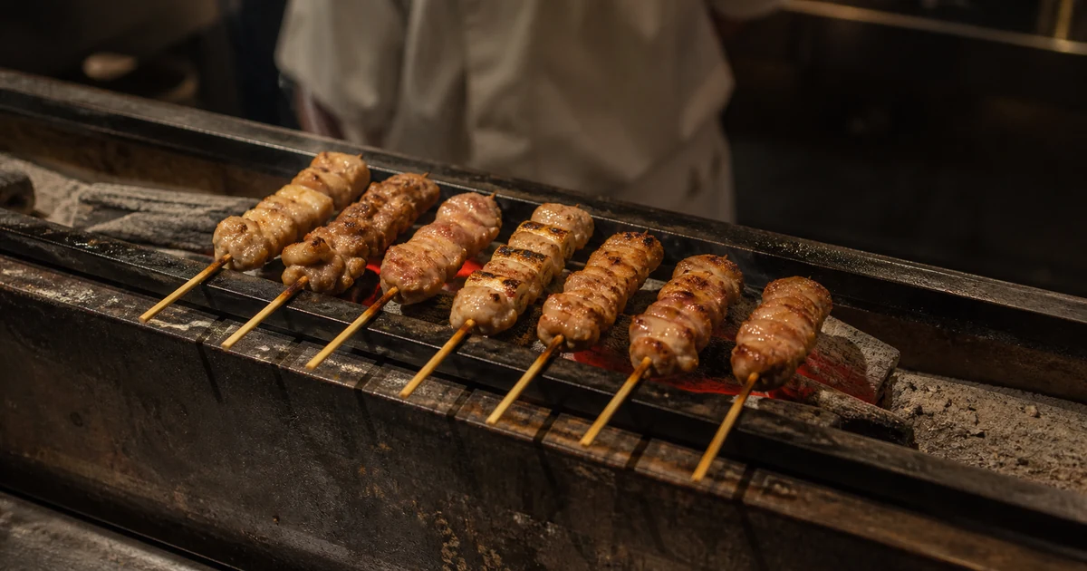 Yakitori skewers cooking over a narrow charcoal grill at a Japanese restaurant