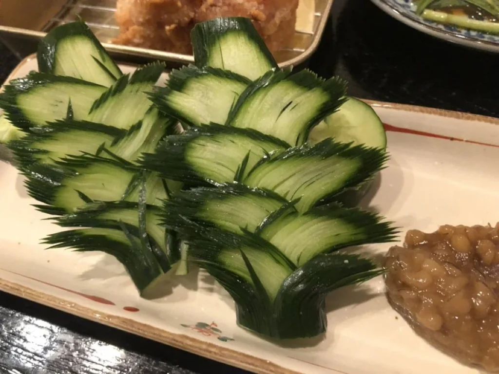 Carved Cucumber Garnish at a Japanese Restaurant Layered fan-shaped cucumber garnishes served beside food at a Japanese restaurant