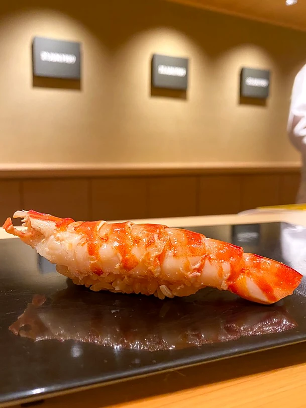 Cooked shrimp nigiri served on a dark plate at a sushi counter