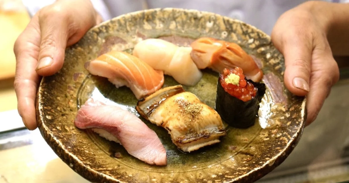 Sushi chef presenting an assortment of nigiri on a ceramic plate
