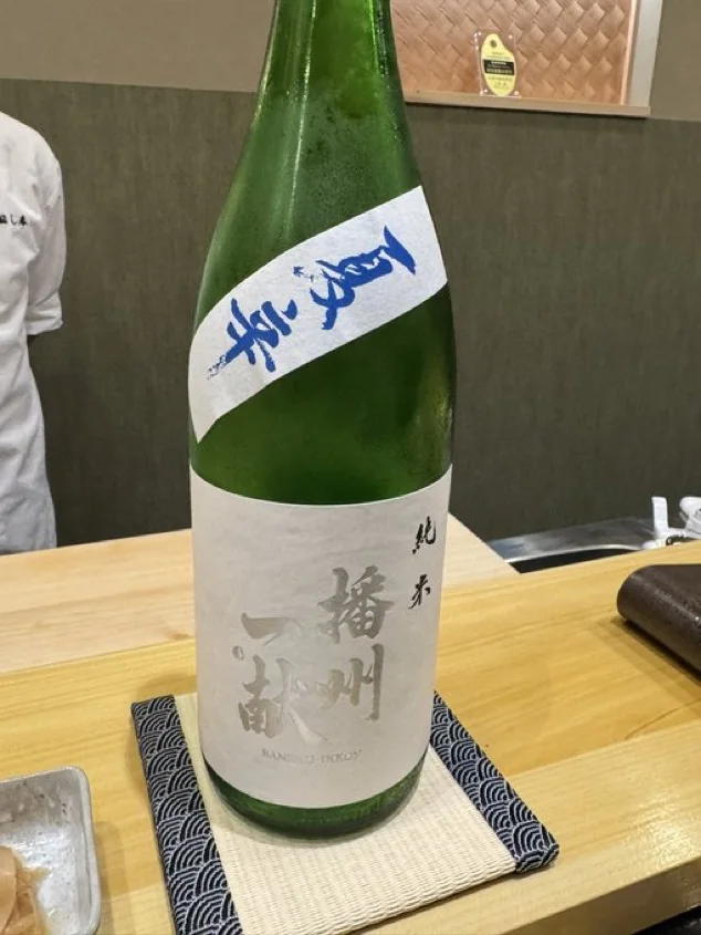 Green sake bottle with the word Junmai visible on its label at a sushi counter