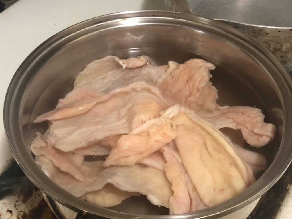 Raw chicken skin in a pot at the beginning of the parboiling process