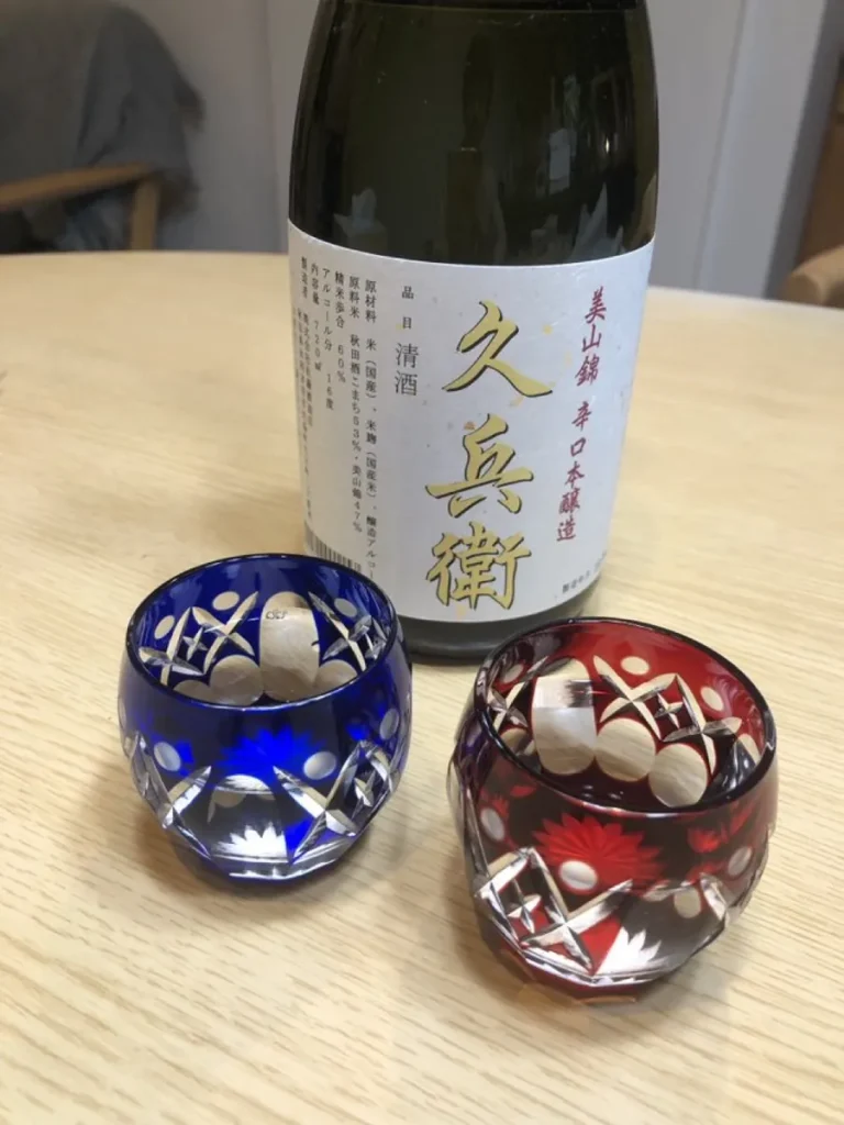 Red and blue cut-glass sake cups beside a Japanese sake bottle
