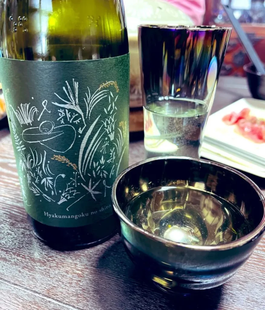 Sake served in a tall glass and a dark bowl beside a bottle