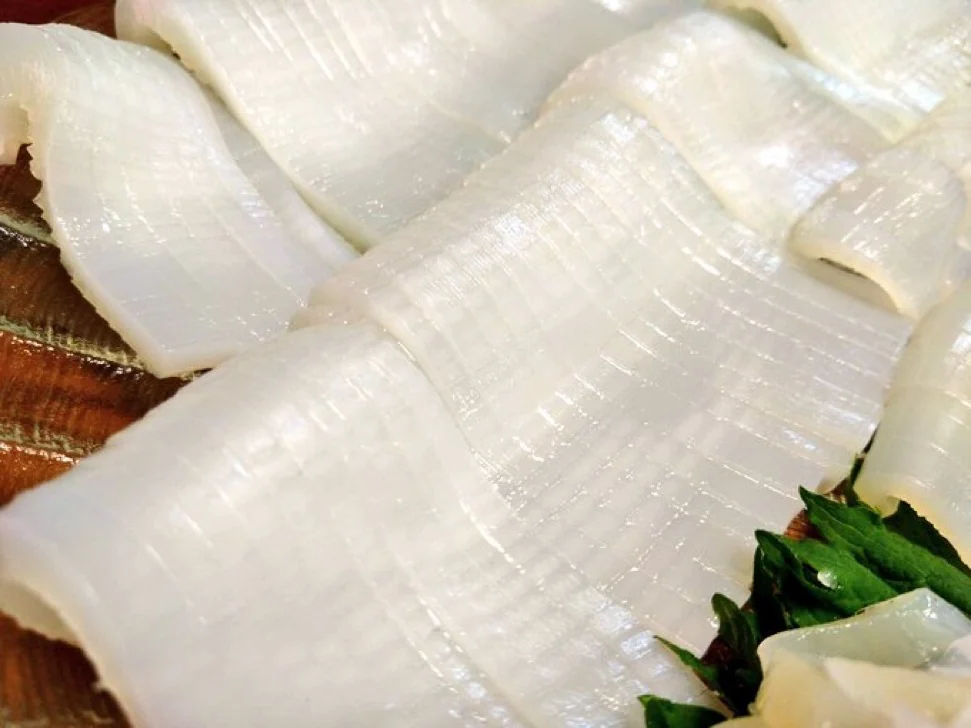 Scored Squid Sashimi With Decorative Knife Cuts White squid sashimi with fine crosshatch knife cuts across the surface