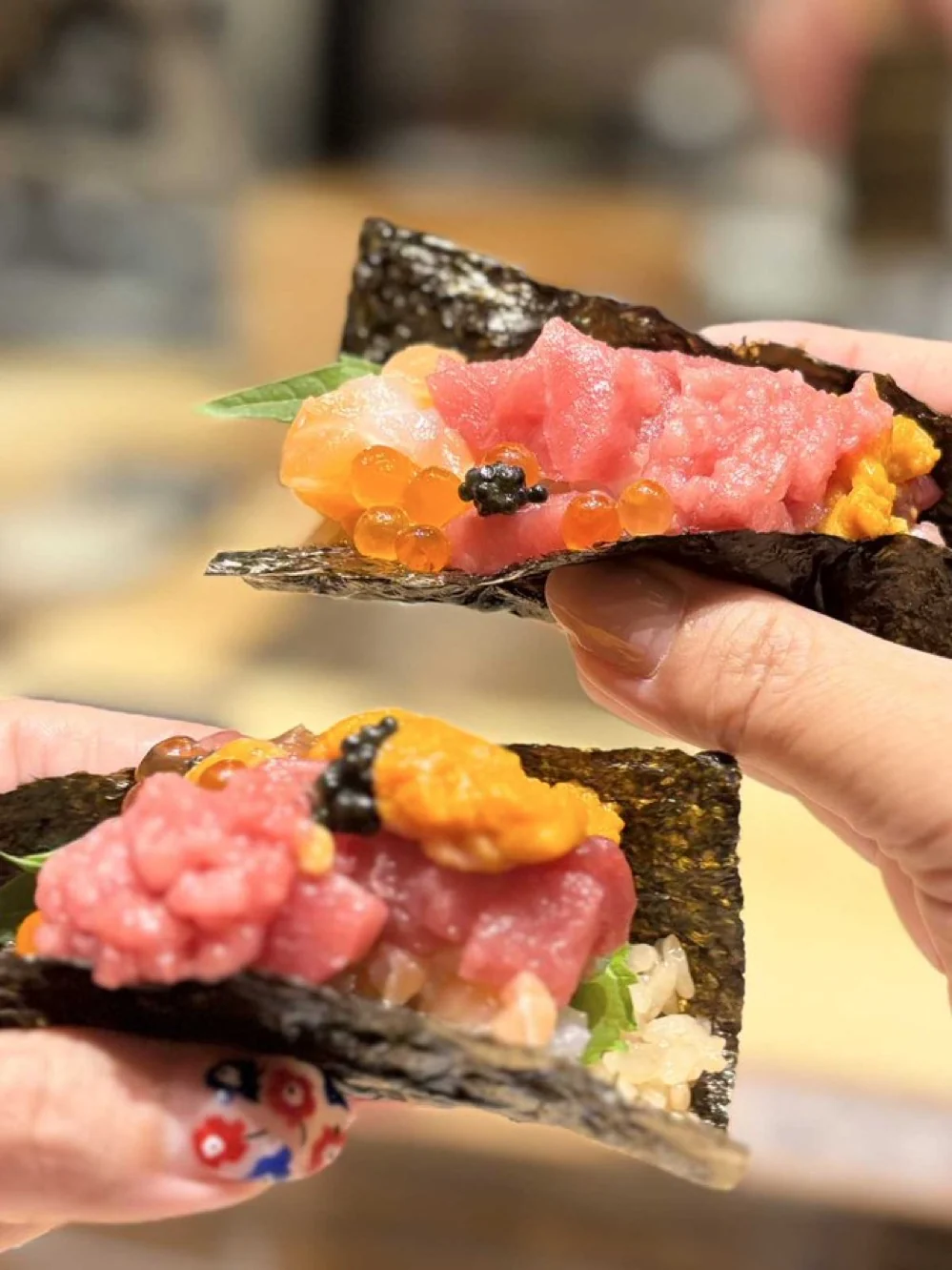 Two diners holding seafood temaki wrapped in crisp nori