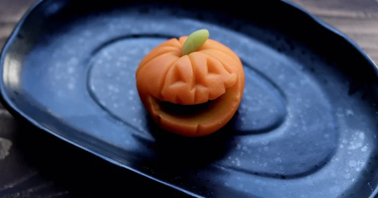 Orange kabocha wagashi shaped like a jack-o-lantern on a black plate