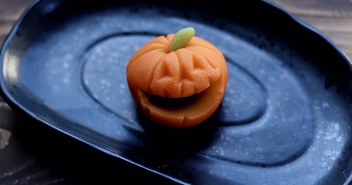 Orange kabocha wagashi shaped like a jack-o-lantern on a black plate