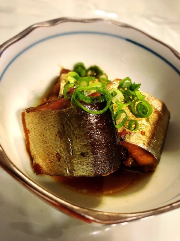 Simmered Sanma With Green Onions Pieces of simmered sanma in a dark savory sauce topped with sliced green onions