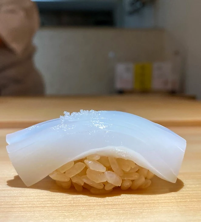 Translucent squid nigiri served on a pale wooden sushi counter