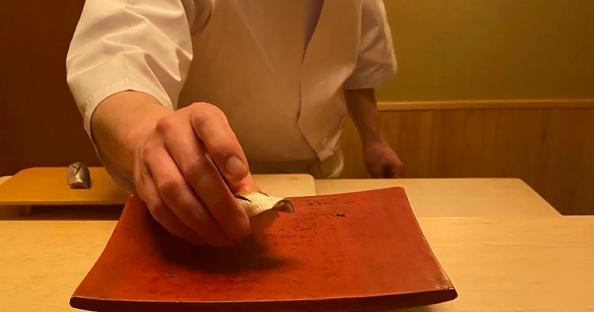 Sushi chef placing a piece in front of a diner at a wooden counter